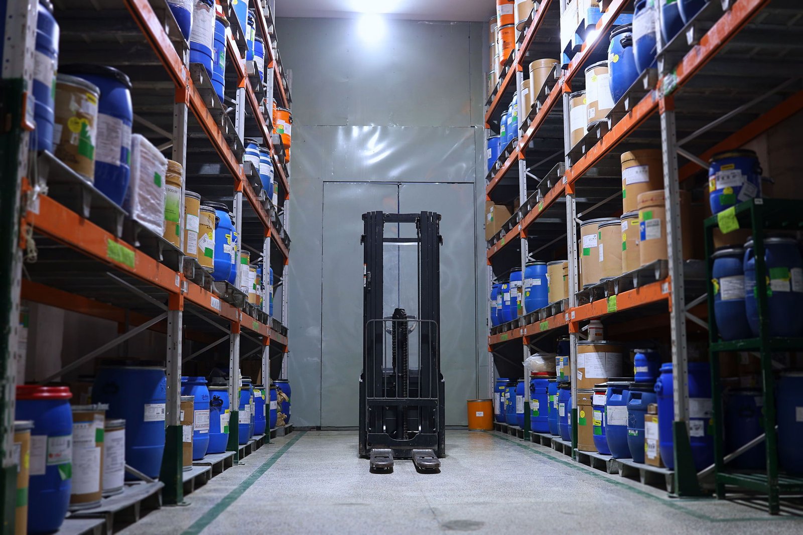 Pasillo de almacén con tambos y bidones de materia prima química acomodados en racks